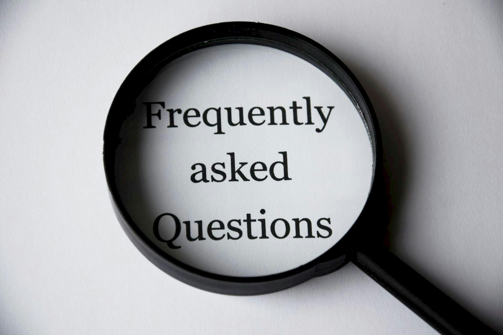 FAQ Close-up of a magnifying glass focusing on the phrase 'Frequently Asked Questions'.
