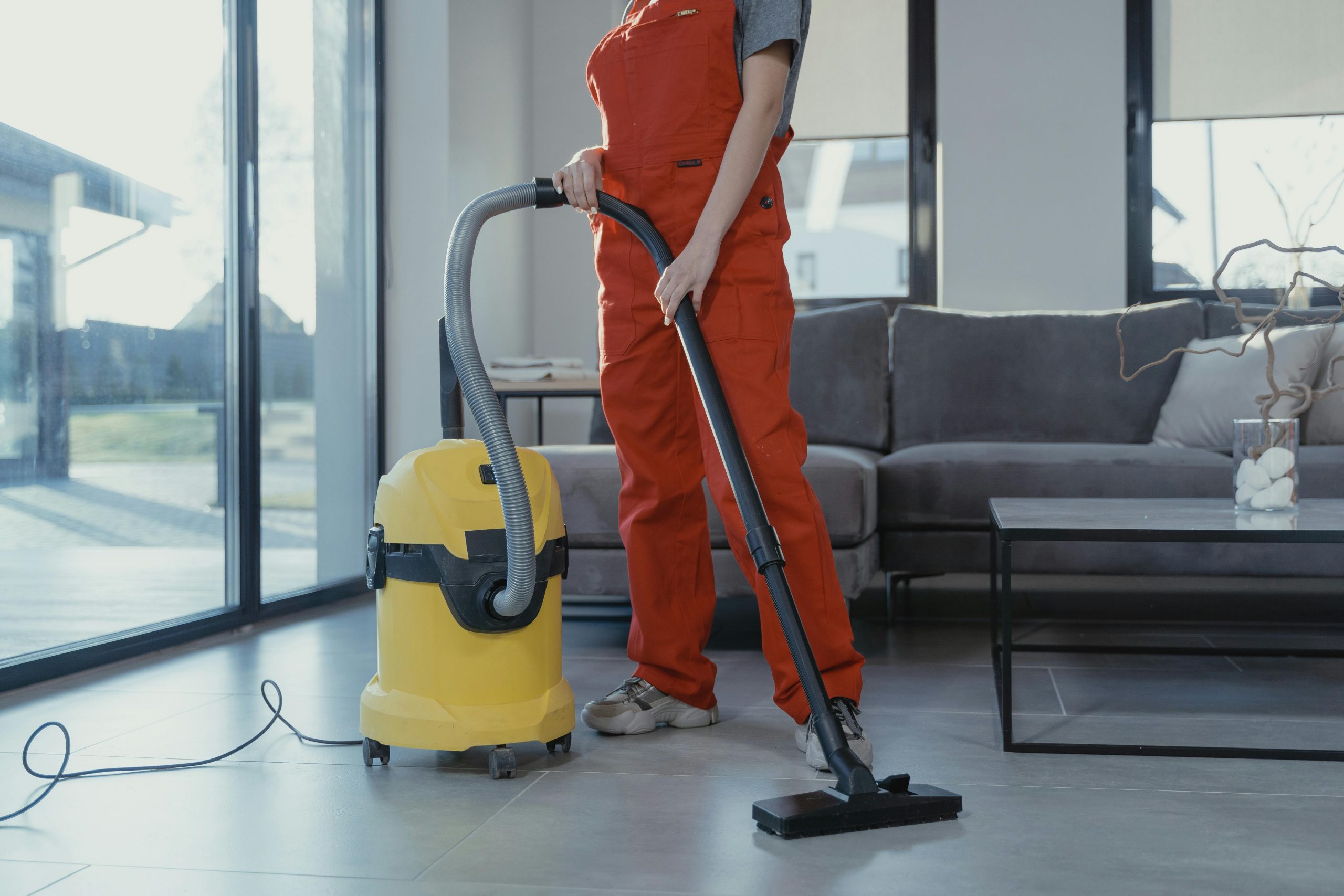 Commercial Cleaning A professional cleaner in red coveralls vacuuming a modern living room with a yellow vacuum cleaner.
